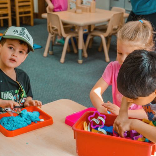 three preschoolers playing with sand and blocks